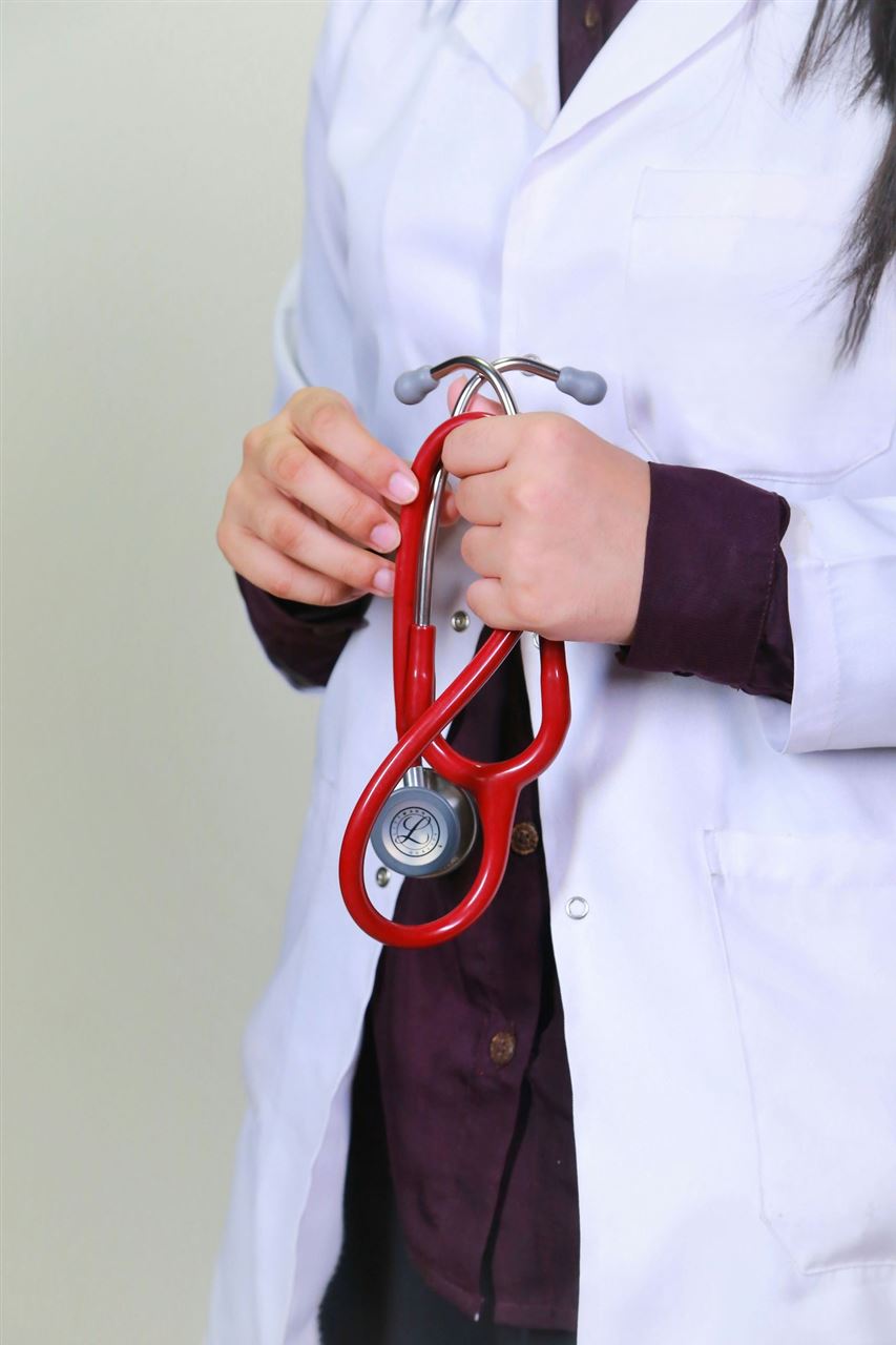 a woman in a white clinician's coat holding a stethoscope in her hands