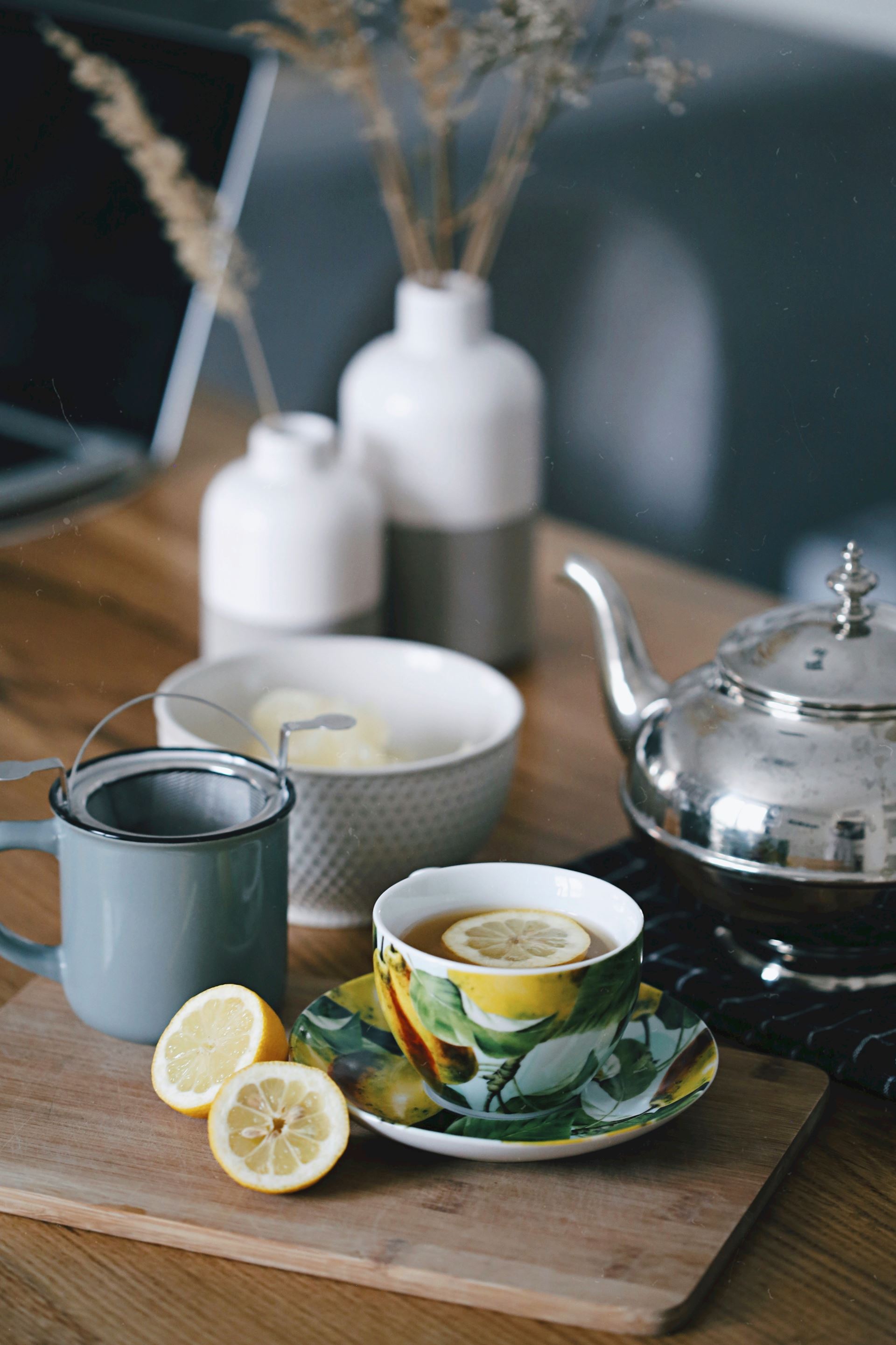a pot of tea, a filled cup and a plate of lemon slices on a table